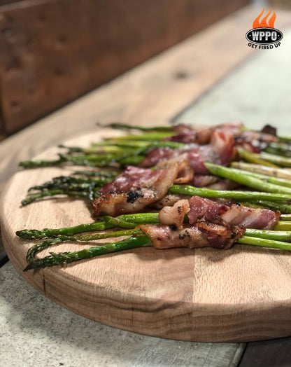 Grilled asparagus spears wrapped with bacon on a wooden cutting board, with WWPO logo in the corner.